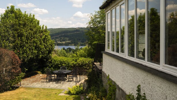 Un patio con mesa y sillas, un sendero de piedra y vistas a un lago y colinas.