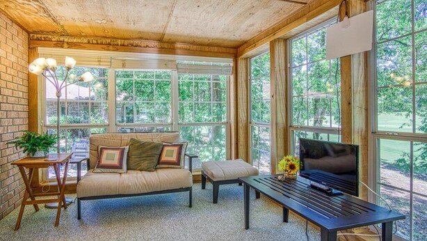 Une pièce confortable avec un canapé, une table basse et un téléviseur. De grandes fenêtres offrent une vue sur la verdure environnante.