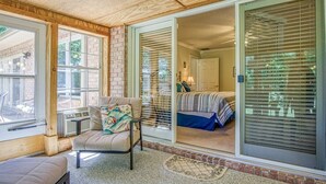 Une pièce chaleureuse avec une porte-fenêtre coulissante donnant sur un balcon, un fauteuil confortable et un lit recouvert d’une courtepointe à rayures.