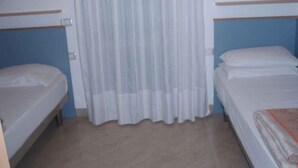 Een kamer met twee bedden, een gordijn en een betegelde vloer.