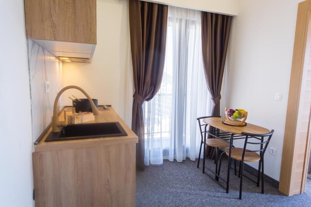 A compact kitchenette with a sink, stove, and wooden cabinets. There is a small dining table with two chairs and a fruit bowl.
