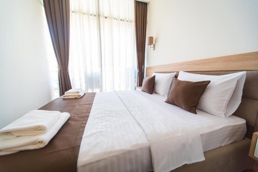 Cama bem arrumada com cabeceira marrom, roupa de cama branca e alguns travesseiros.