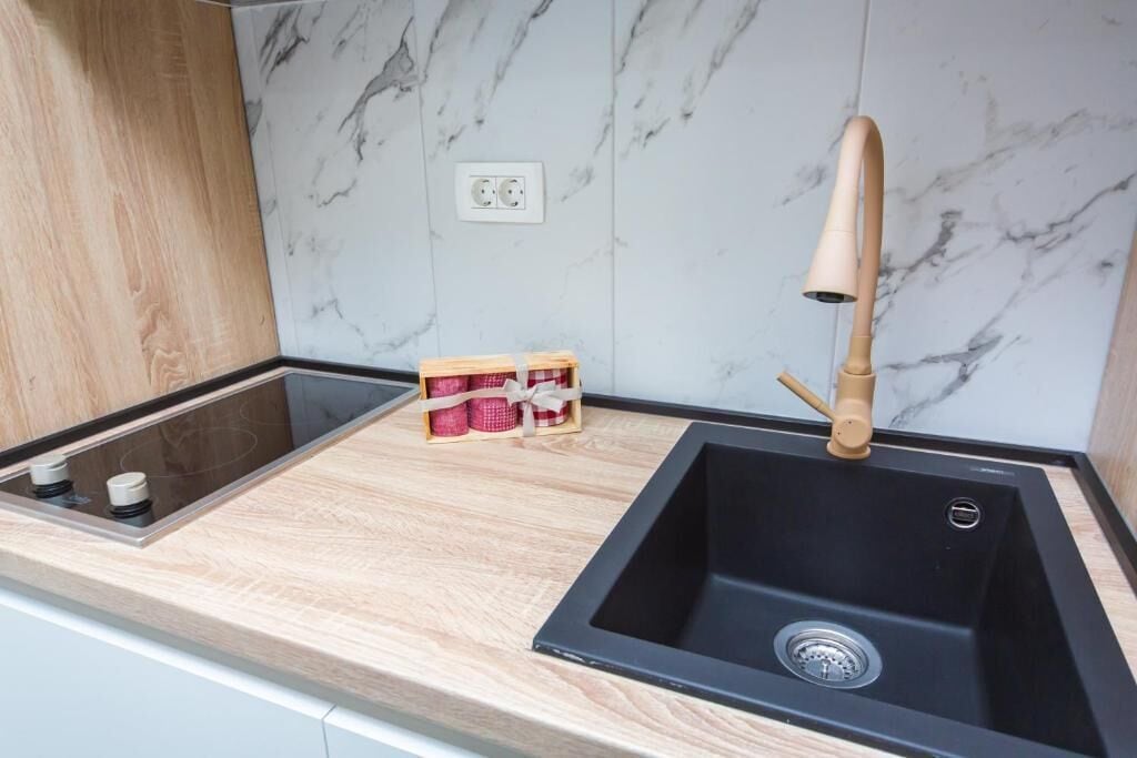 Una cocina moderna con un lavamanos negro, encimera de madera, salpicadero de mármol y un pequeño cofre de madera con objetos rojos y blancos.
