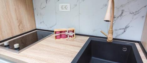 Una cocina moderna con un lavamanos negro, encimera de madera, salpicadero de mármol y un pequeño cofre de madera con objetos rojos y blancos.