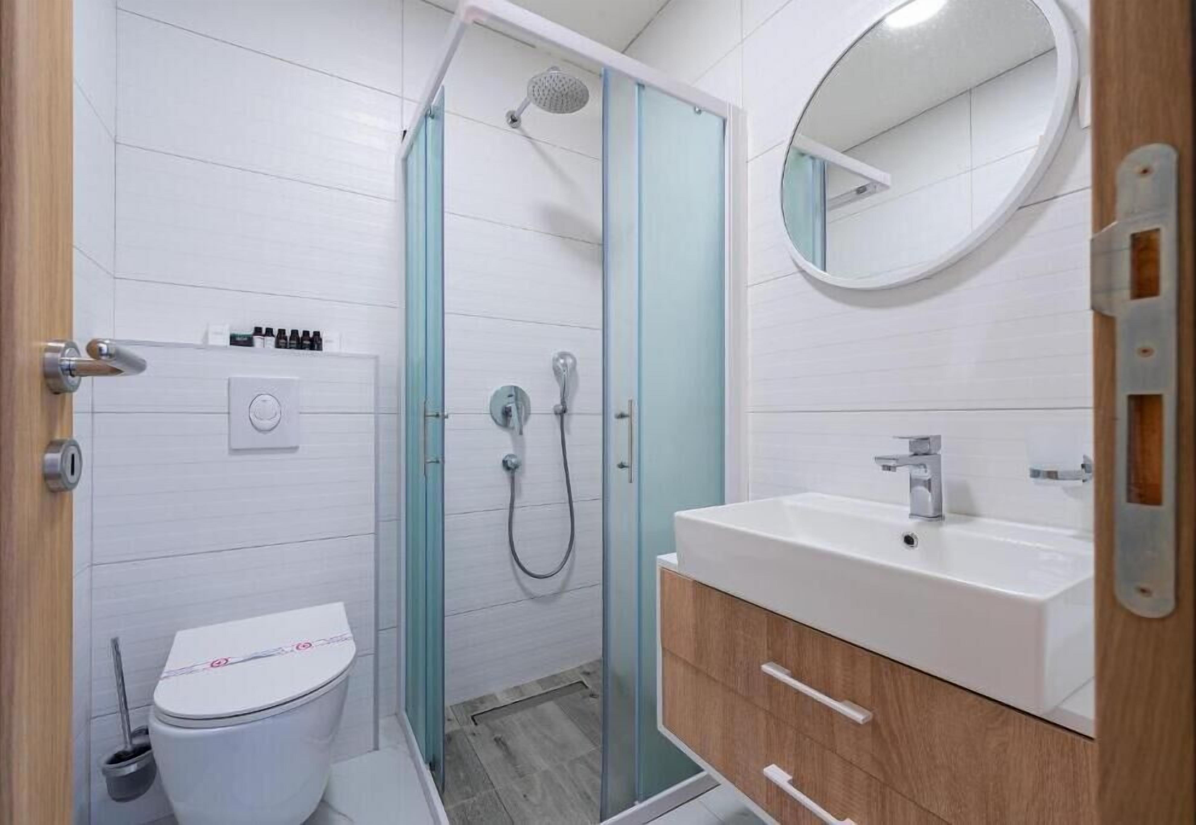Un baño moderno con ducha de vidrio, lavamanos blanco y tocador de madera.