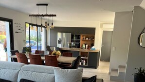 A modern living room with a large sectional sofa, a dining area with a table and chairs, and a kitchen in the background.