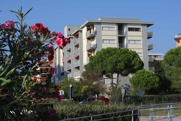 Un immeuble résidentiel à plusieurs étages, doté de balcons, entouré de verdure et surplombant un ciel dégagé.