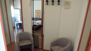Ein Zimmer mit zwei Karo-Sesseln, einem Bett mit weißem Kopfteil und einem Spiegel, der ein Bett und ein Gemälde reflektiert.