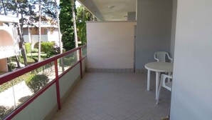 Ein Balkon mit roter Geländer, einem weißen Tisch und Stuhl sowie Blick auf ein Gebäude und Bäume.