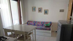 Eine kleine Küche mit Esstisch und Stühlen, ein Sofa mit bunten Kissen und ein Kühlschrank.