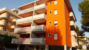 A multi-story building with balconies, a flat roof, and a clear sky. - Holiday apartment the sea with air conditioning (Bibione)