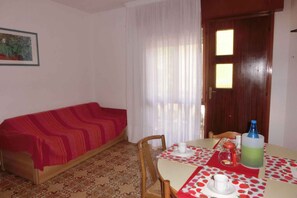 A room with a red sofa, a dining table with a red and white tablecloth, chairs, and a wooden door with windows.