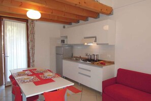 A compact kitchen with a dining table, chairs, and a red sofa.