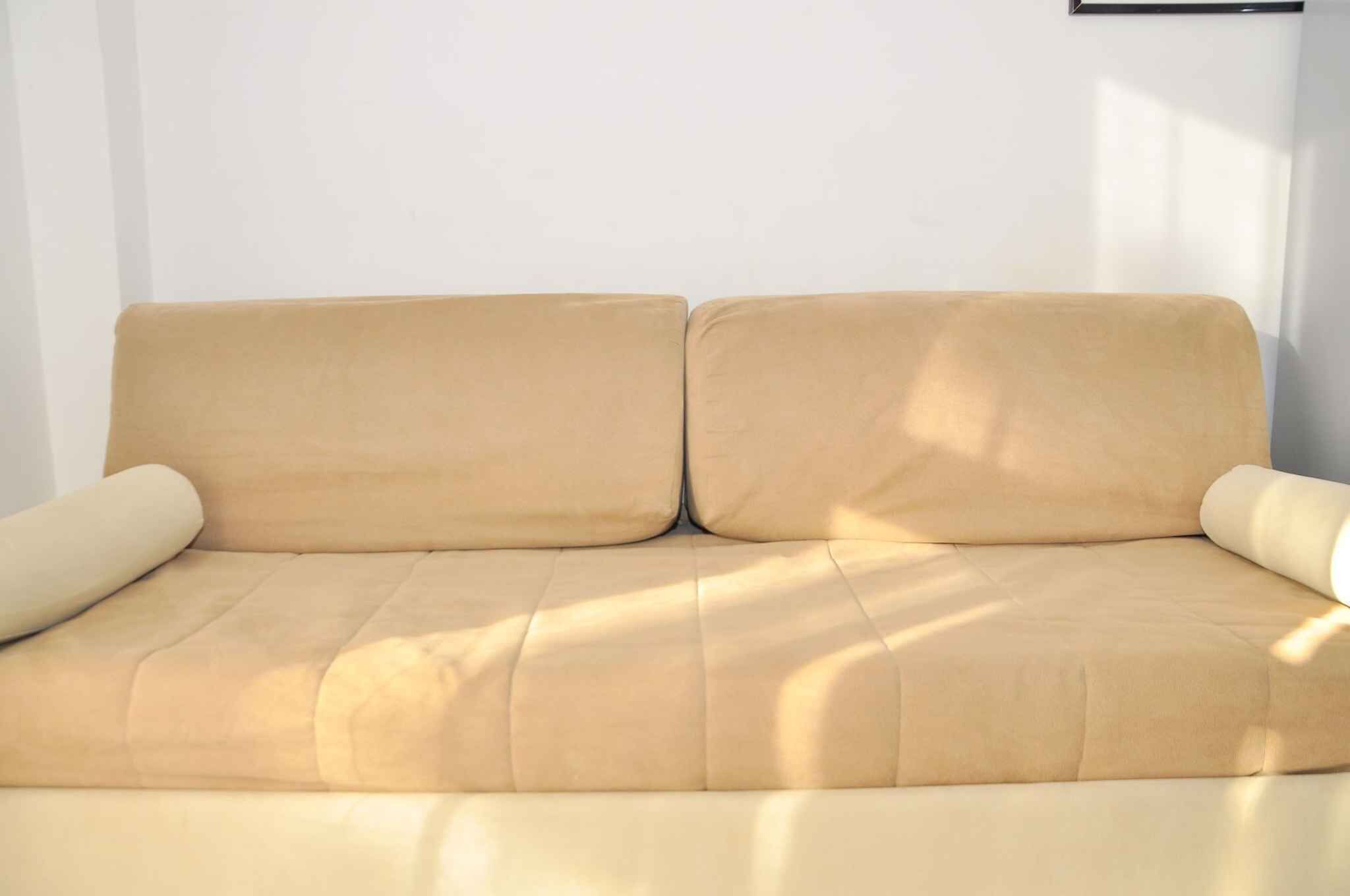 A beige sofa with a cushion on each side, positioned against a white wall.