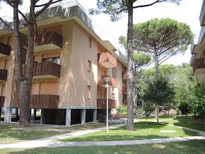 A multi-story building with balconies, surrounded by trees and a well-maintained lawn. - Holiday apartment mit Klimaanlage und Balkon (Bibione)