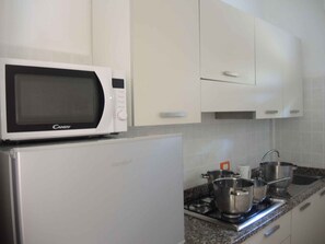 Uma cozinha equipada com micro-ondas, geladeira, fogão e panelas.