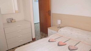 A bedroom with a bed, a bedside table with a lamp, a wardrobe, and a door. - Holiday apartment mit Klimaanlage und Balkon (Bibione)