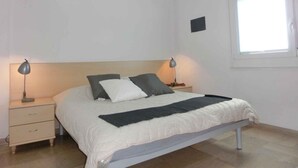 A bedroom with a bed, two bedside tables, a window, and a small wall-mounted shelf. - Holiday apartment near the sea (Bibione)
