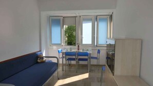 A room with a blue sofa, a dining table with chairs, and a kitchen area. - Holiday apartment near the sea (Bibione)