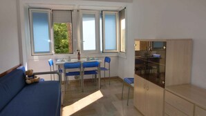 A room with a dining table, chairs, a sofa, and a cabinet. - Holiday apartment near the sea (Bibione)