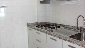 A kitchen with white cabinets, a granite countertop, stainless steel sink, and a gas stove. - Holiday apartment near the sea (Bibione)