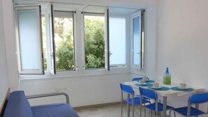 A hospital room with a bed, a table with chairs, and windows with a view of greenery. - Holiday apartment near the sea (Bibione)