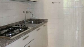 A kitchen with white cabinets, a gas stove, a sink, and a tiled backsplash. - Holiday apartment near the sea (Bibione)