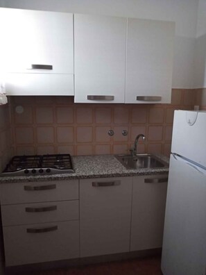 Una cocina con estufa a gas, pileta y alacenas blancas.