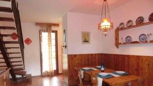 Un comedor con mesas y sillas de madera, una escalera y un estante en la pared con platos.