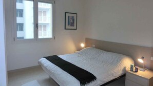Een slaapkamer met een bed, nachtlampjes, een nachtkastje, een raam en een ingelijste foto aan de muur.