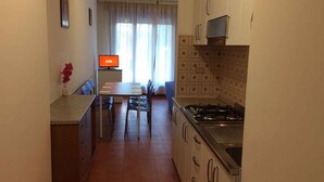 Cocina compacta con comedor, televisor y ventana con cortinas.