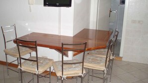 Un comedor con una mesa de madera y seis sillas, un televisor montado en la pared y un baño al fondo.