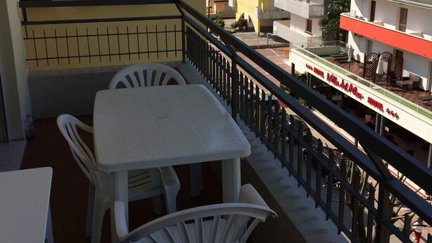 A balcony with a table and chairs, a railing, and a view of surrounding buildings. - Holiday apartment mit Klimaanlage und Balkon (Bibione)