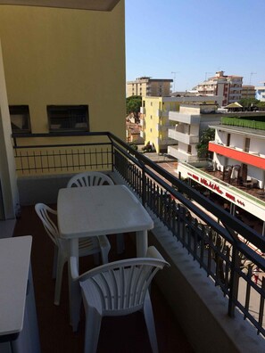 Un balcon avec une table et des chaises, une balustrade et une vue sur les bâtiments environnants.