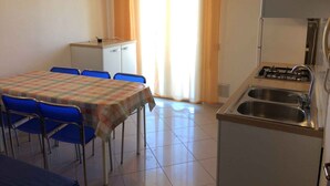 A small kitchen with a gas stove, sink, and a dining area with a table and chairs. - Holiday apartment mit Klimaanlage und Balkon (Bibione)