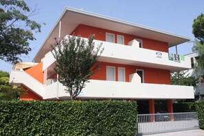 Un bâtiment à deux étages avec une façade rouge et blanche, un balcon et un arbre devant.