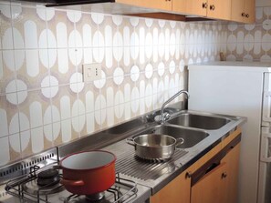 A kitchen with a gas stove, two sinks, and patterned tiles.