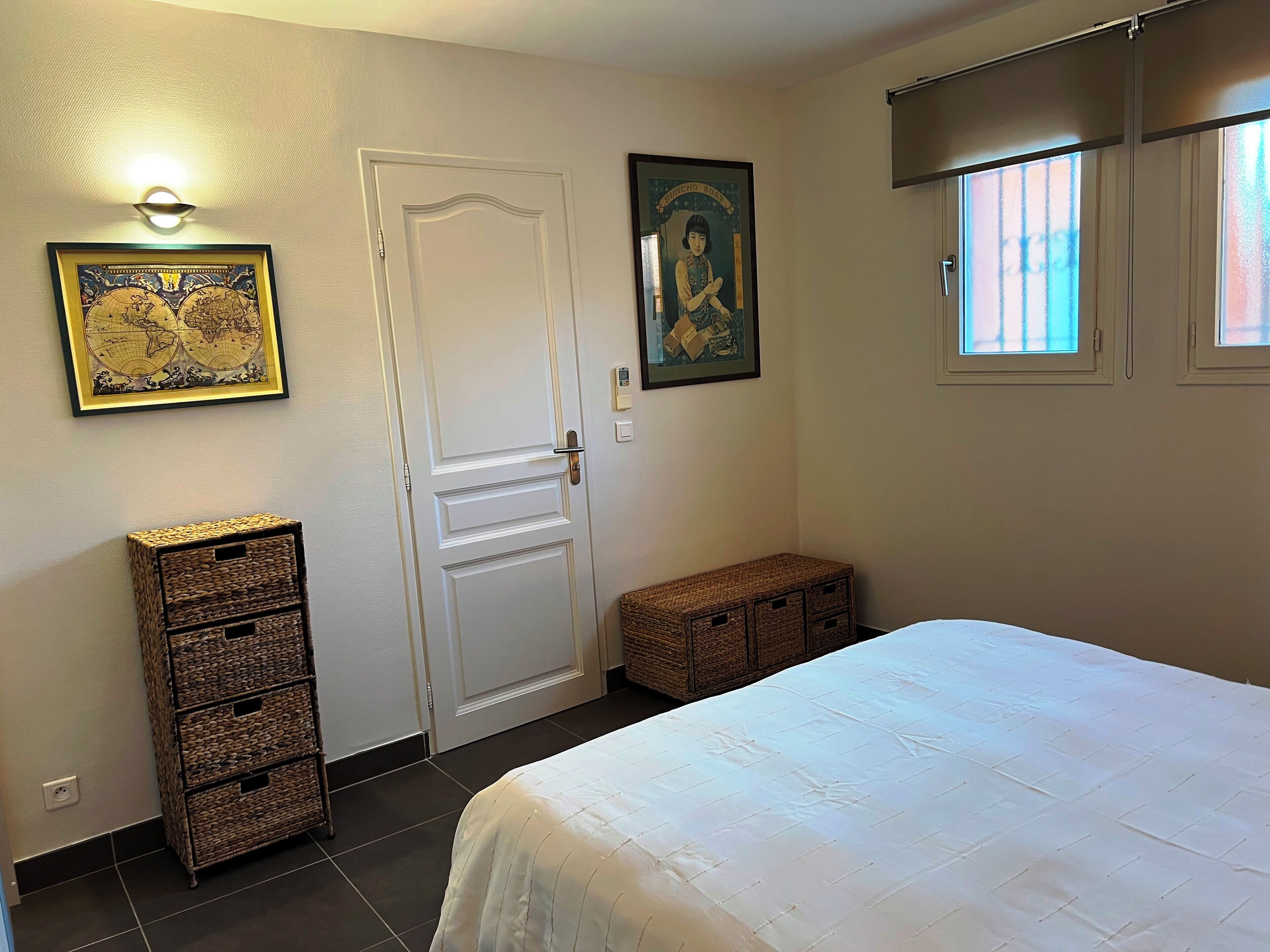 Una camera da letto con un letto, una porta, cesti di vimini, una mappa del mondo incorniciata e un quadro appeso alla parete.
