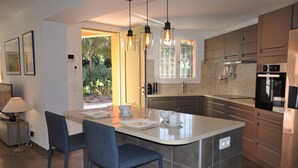 Een moderne keuken met een centraal eiland, barstoelen, hanglampen en roestvrijstalen apparatuur.