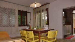 Un coin repas avec une table en bois et des chaises jaunes, un luminaire suspendu et une fenêtre avec des rideaux.