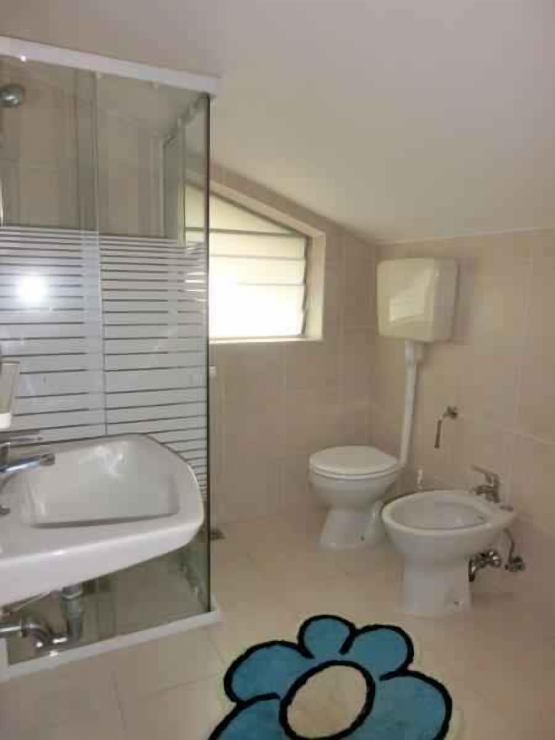 A bathroom with a sink, toilet, bidet, and a window.