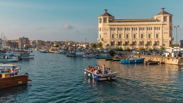 Un port de plaisance avec des bateaux amarrés et, au fond, un grand bâtiment à l’architecture classique.
