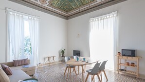 A spacious living room with a large round table, a sofa, and a television. The room has patterned floor tiles and a decorative ceiling. - Casa Darsena with Sea View Balcony by Wonderful Italy (Siracusa)