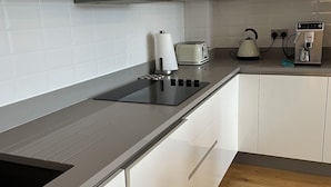 Een moderne keuken met witte kasten, een zwart aanrecht, een waterkoker, een broodrooster en een koffieapparaat.