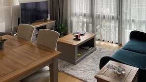 Een moderne woonkamer met een houten eettafel, twee stoelen, een bank, een televisie en een salontafel.