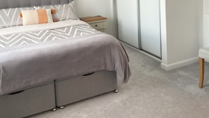 Een moderne slaapkamer met een grijs gestoffeerd bed, een nachtkastje en een schuifdeurkast.