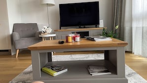 Een moderne woonkamer met een houten salontafel, een grijze bank, een televisie en een lamp.