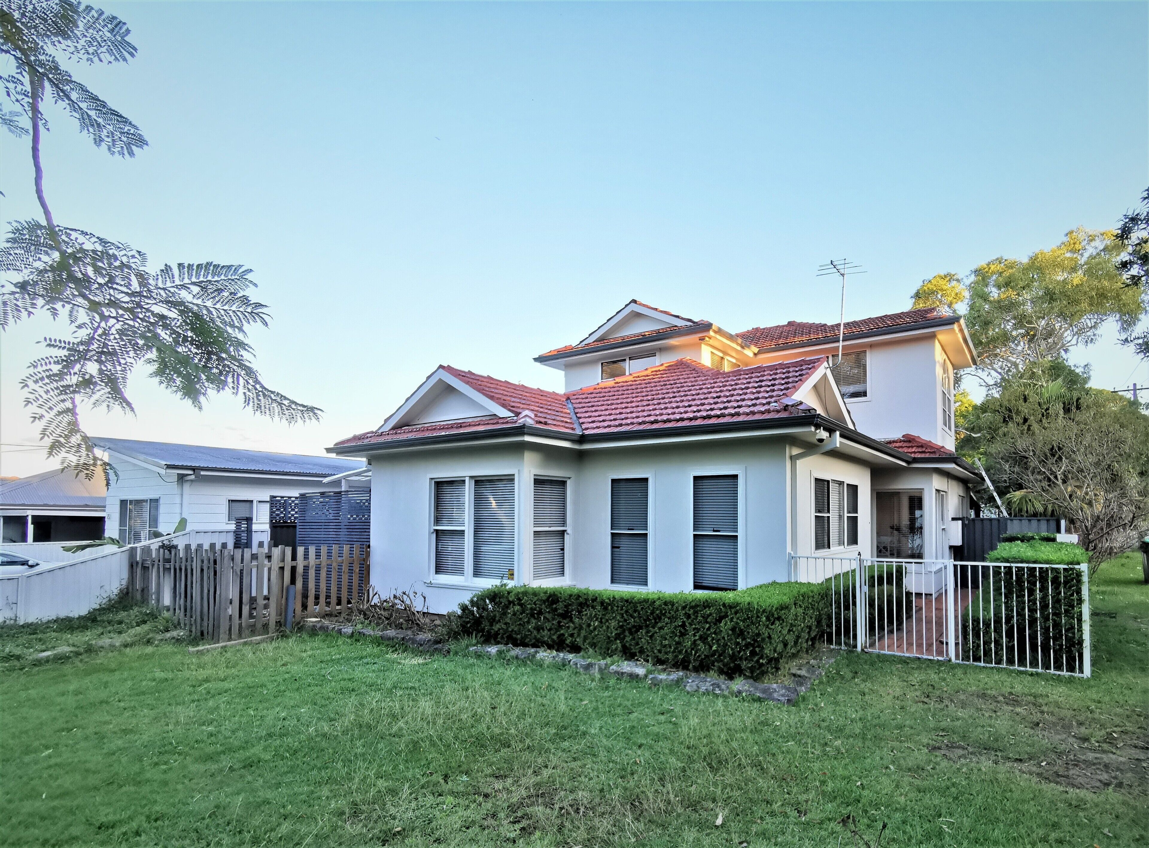 A two-story house with a red-tiled roof, white exterior walls, and a fenced yard.