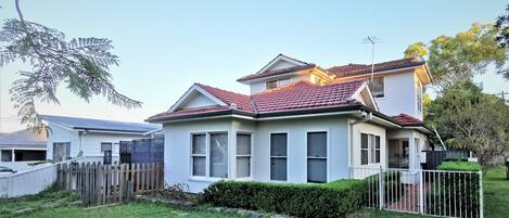A two-story house with a red-tiled roof, white exterior walls, and a fenced yard.