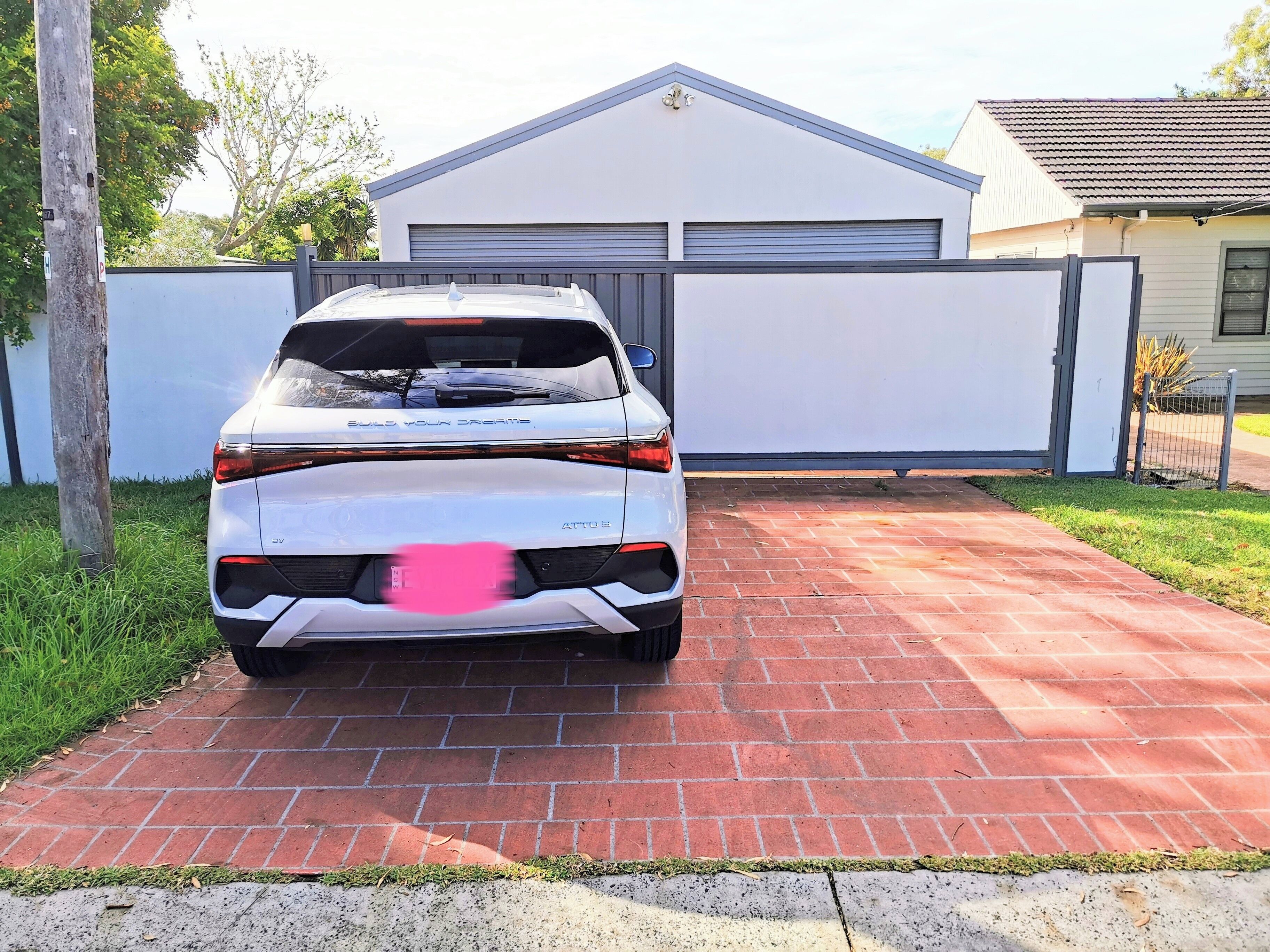 Une voiture blanche est garée sur une allée pavée de briques devant un garage.